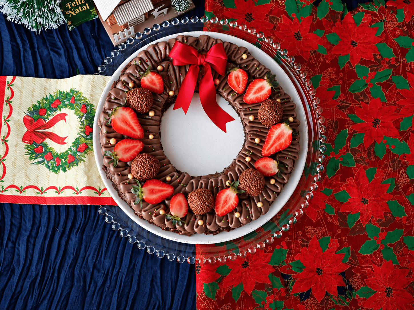 Bolo de brownie em formato de guirlanda, decorado com morangos, brigadeiros e um laço vermelho
